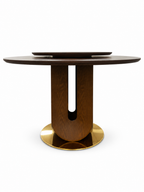 Low front view of the Vincennes Round Wood Dining Table, showing its wooden tabletop and raised turntable, curved U-slot pedestal and circular gold-tone base on white.