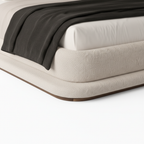 Kendric Bed close-up of cream fabric headboard, white pillows, and black throw